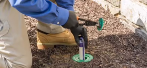 Pest control technician installing a termite bait station in mulch along a stone foundation wall in Pittsburgh